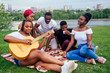 © yurakrasil - Group of smiling happy afro-american friends friends playing guitar outdoors picnic in the campaign