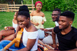 © yurakrasil - Group of smiling happy afro-american friends friends playing guitar outdoors picnic in the campaign