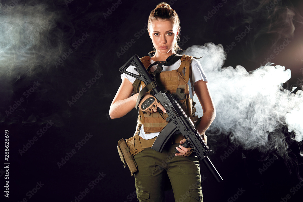 Woman in the army pros and cons. Women do not just serve, but attain high positions and ranks. Beautiful woman in military outfitholding weapon in hands stands in smoky background