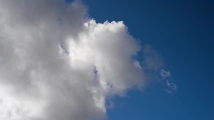 Wall Mural - Time-lapse of dynamic, fluffy white and grey clouds moving through a colorful misty blue sky