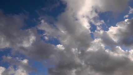 Wall Mural - Time-lapse of dynamic, fluffy white and grey clouds moving through a colorful misty blue sky