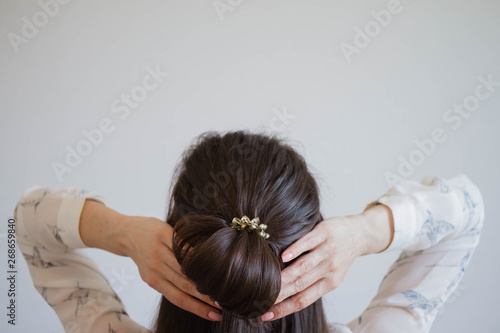A Young Woman With Brown Hair Ties Her Hair Into A Bun Viewed