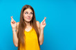 Young woman with long hair over isolated blue wall with fingers crossing and wishing the best