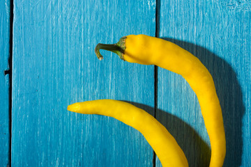 two yellow chili peppers on blue wooden table background