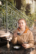 © New Africa - Young woman enjoying tasty coffee while using mobile phone at table outdoors
