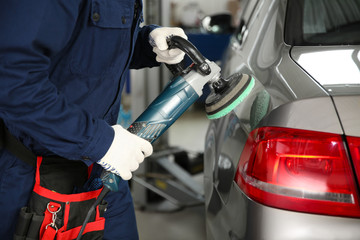 Technician polishing car body with tool at automobile repair shop, closeup