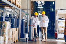 Smiling Young Caucasian Employee Transporting Bottle With Gas While Manager Holding Tablet And Talking To Worker. Warehouse Interior.