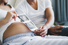 Young Asian Couple Holding Ultrasound Film Of Their Baby On White Bed