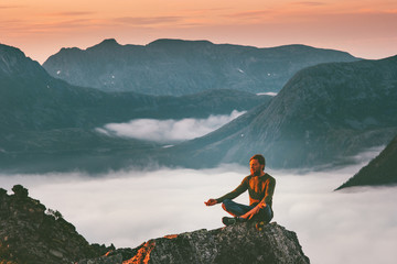 Wall Mural - Yoga meditation in mountains man traveler relaxing alone lotus pose above clouds summer vacations outdoor harmony with nature tranquil scene