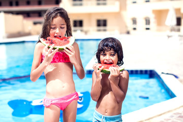 Little boy and girl eat watermelon at the swimming pool. Children and summer concept