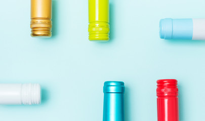 Wall Mural - Screw bottle foil caps in different bright colors of white and rose wine bottles on blue background with copy space. Minimal abstract colorful mockup concept of alcohol beverage. Flat lay.