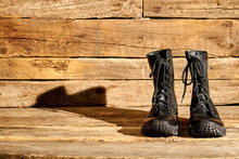 Black Combat Army Boots On Wood. Shiny Shoes With Shadow.