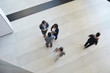 © Seventyfour - Directly above view of intercultural business colleagues in formalwear standing in lobby of company and chatting during break while another employees being in hurry, blurred motion effect