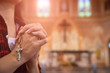 Woman hand holding rosary against cross and praying to God at church.