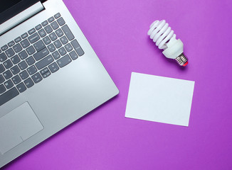 Wall Mural - Modern laptop, spiral light bulb and sheet of white paper for copy space on a purple background. Idea concept. Top view