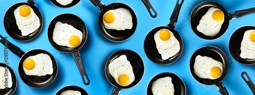 Fotografía Creative food pattern with fried eggs on pans over blue background