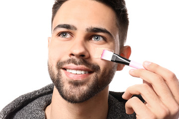 Wall Mural - Handsome man applying clay mask onto his face against white background