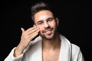 Wall Mural - Handsome man applying clay mask on his face against dark background