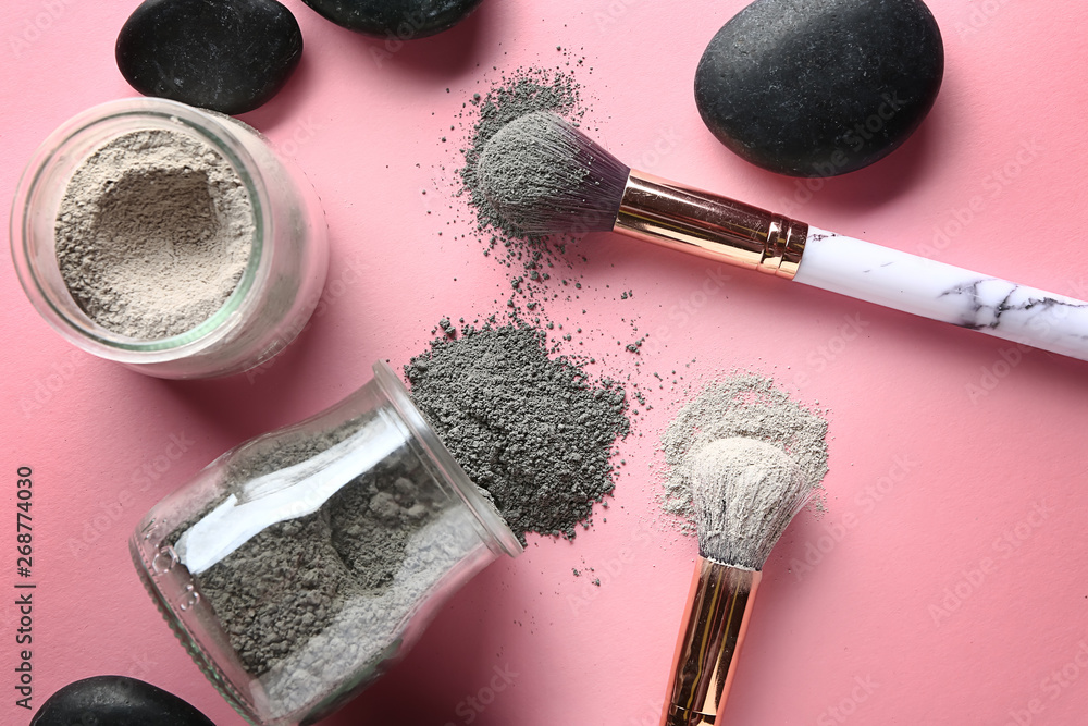 Jars with cosmetic clays and brushes on color background