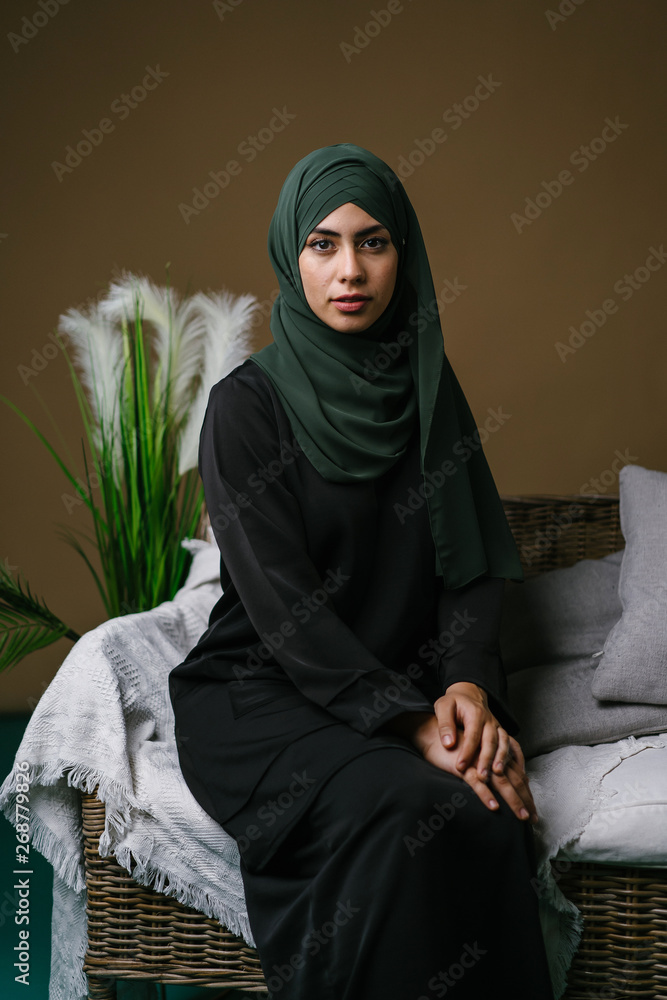 Photo Stock Portrait of a beautiful, elegant and attractive young  Indonesian Asian Muslim woman in a black dress and an olive green hijab  head scarf. She has a neutral expression as she