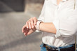© Viktoria - Woman wearing white shirt wearing blue jeans and a gentle nude manicure looks at the watch close-up