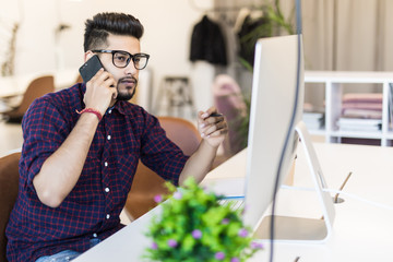 Indian freelancer man working on laptop and talking on the phone