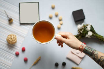 on a blue background sprig flower black berries blueberries and red white marshmallows gray envelope pink butterfly writing tablet and business card hand with tattoos holding a mug of tea