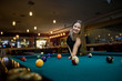 © RomanR - Young and beautiful woman in pub playing billiard