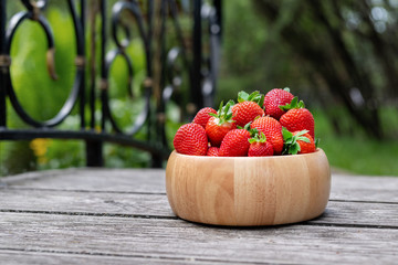 Sweet fresh juicy organic ripe strawberries in wooden bowl on wooden surface outdoors in garden or backyard