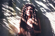 © olezzo - Young beautiful sensual brunette girl with dreadlocks on the background of the wall and the shadow of palm leaves on her face