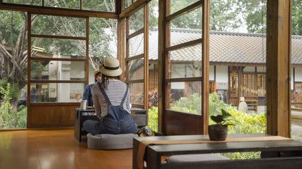 back view of two asian women relaxing on summer vacation fun mood kyoto japan. ladies travelers sitting by window chatting talking enjoy spring garden view outdoor wooden japanese house interior.