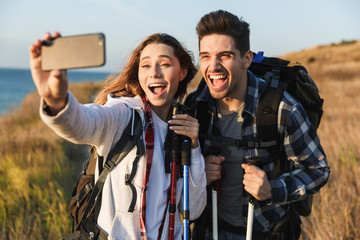 Wall Mural - Cheerful young couple carrying backpacks hiking together