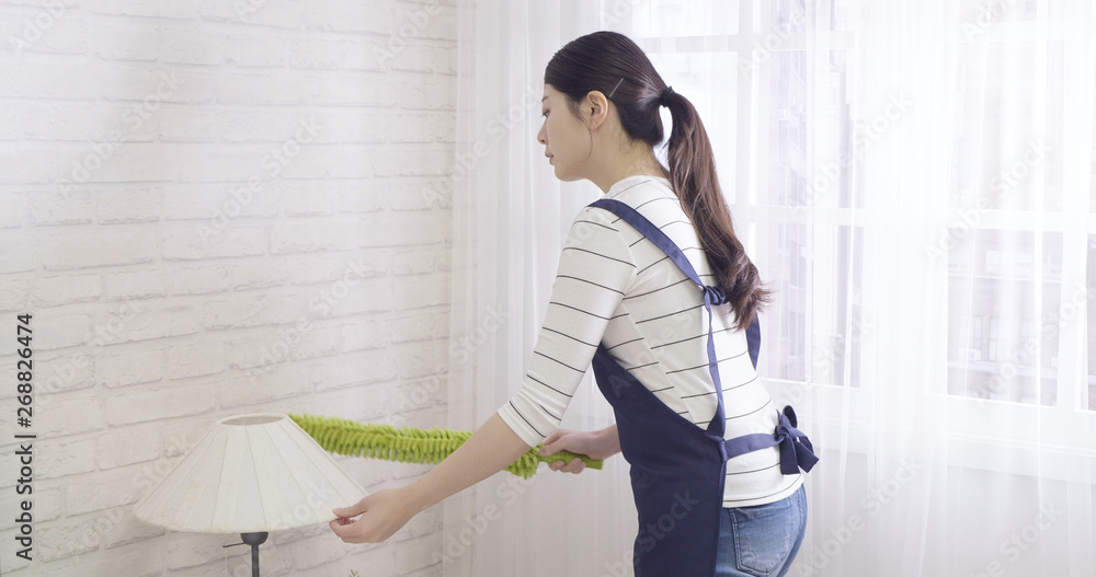 elegant young asian housewife cleaning lamp on nightstand by duster in ...