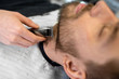 © Syda Productions - grooming and people concept - man and barber with trimmer or shaver cutting beard at barbershop