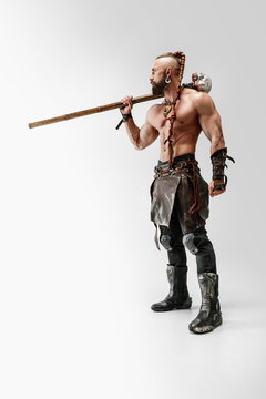 Serious long hair and muscular male model in leather viking's costume with the big mace cosplaying isolated on white studio background. Full-length portrait. Fantasy warrior, antique battle concept.