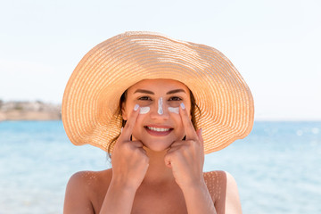 Smiling woman in hat is applying sunscreen on her face. Indian style