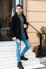 Poster - Photo of attractive man holding paper cup of takeaway coffee while walking through city street