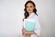 © Christina Moroz - Young attractive professional female doctor in white medical jacket isolated on white background. Brunette woman cosmetologist holding books, notebook, folder. Copy space