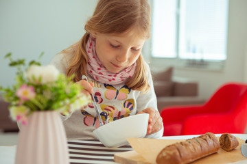 cute little girl eating soup with whole grain bread at home