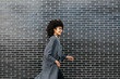 © guille Faingold/Stocksy - Successful stylish woman with afro walking along the street against brick wall.