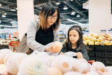 Adorable Girl And Her Mom Choosing Fruit In Supermarket