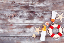Sunscreen Bottles With Seashells And Lifebuoy On Wooden Table