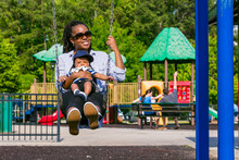 Smiling Mother And Baby Son On Playground Swing