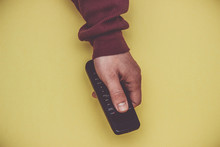 Hand with remote control on a yellow background.