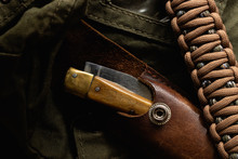 A folding knife in a leather case with a paracord bracelet. Military or hunting themed still life image.