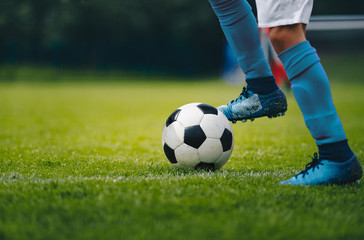 Wall Mural - Close up of legs and feet of football player in blue socks and shoes running and dribbling with the ball. Soccer player running after the ball. Sports venue in the background