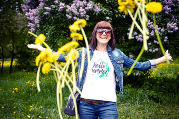 Wall Mural - Woman with dandelions in a green spring park outdoors. Young female with yellow dandelions.