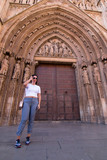 Fototapeta Na drzwi - A young brunette woman walking in front of the Cathedral of Valencia (Spain) with white shirt and gray pants