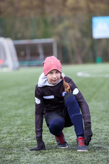 Girl soccer player straightens leggings in football boots, sitting on green field