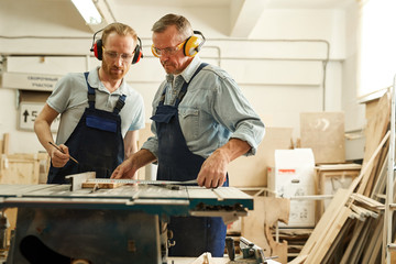 Wall Mural - Waist up  portrait of senior carpenter working with apprentice in joinery workshop, copy space